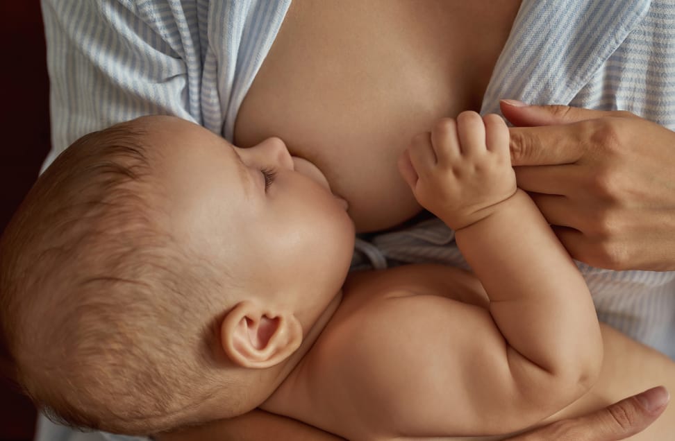 Frischgeborenes Baby trinkt an der Brust und hält Finger der Mutter