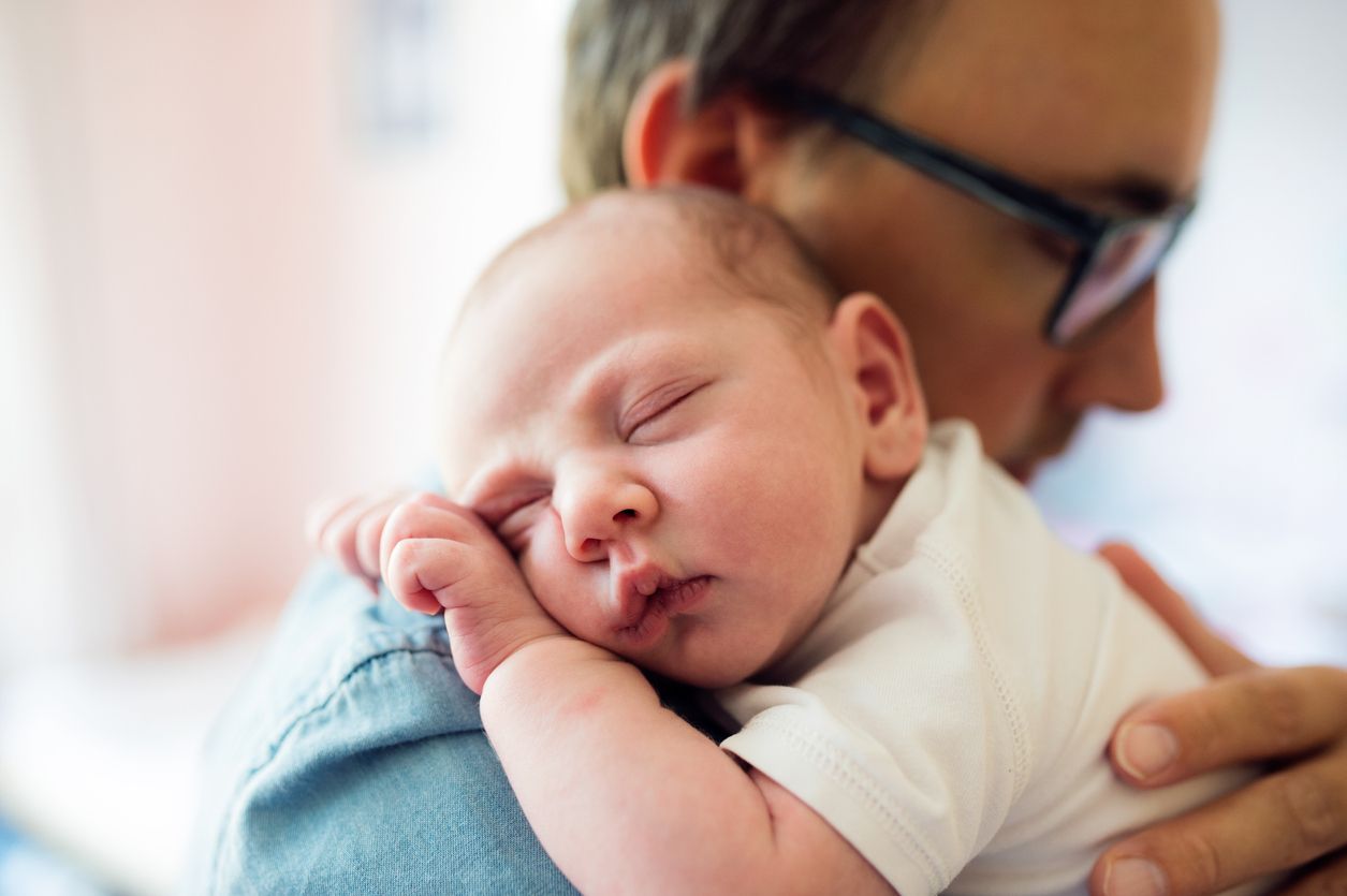 Vater hält neugeborenes Baby auf dem Arm und streichelt es am Rücken